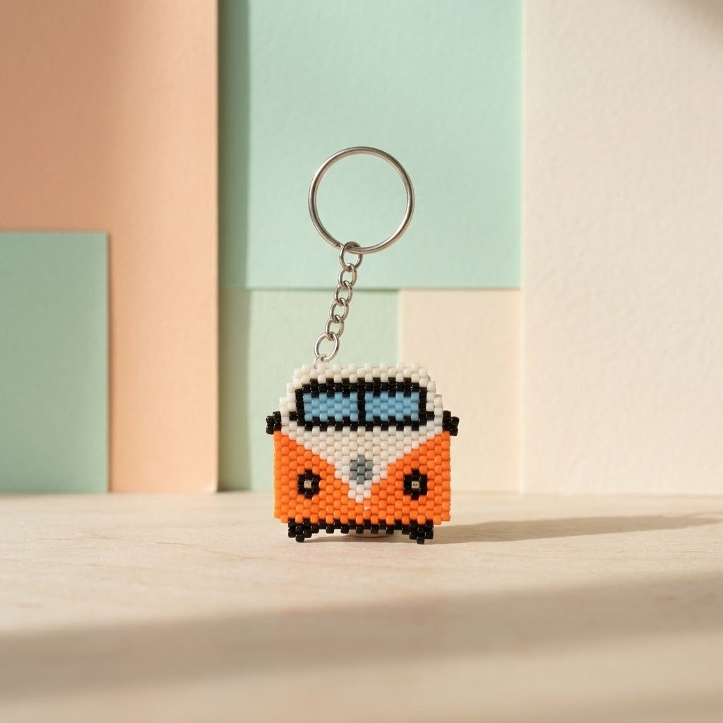 A handmade beaded keychain shaped like a retro orange and white van, featuring a silver metal key ring and chain, displayed on a light wooden surface with pastel geometric blocks in the background.