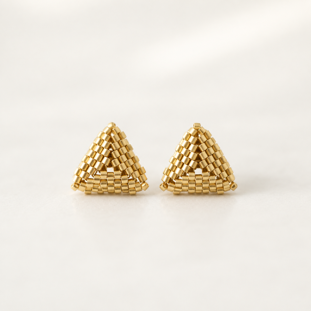 A pair of gold triangular beaded earrings with a textured, woven geometric pattern, displayed on a clean white background.