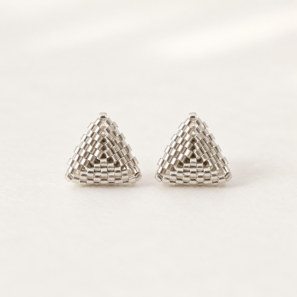 A pair of silver-toned triangular stud earrings made from tightly woven small beads, shown on a clean white background.