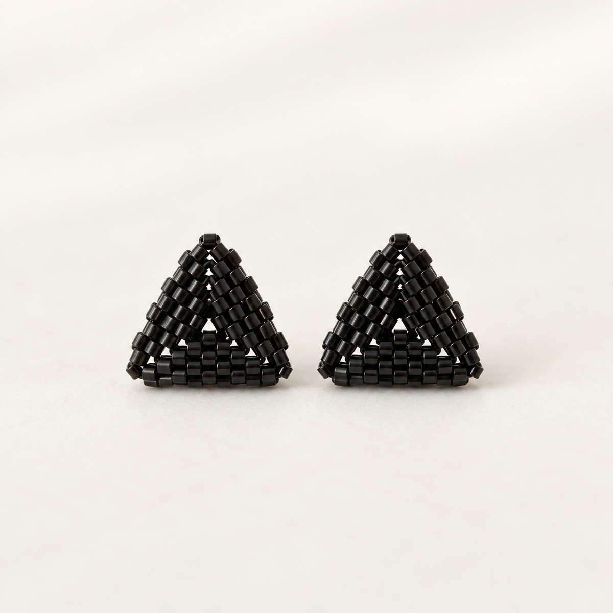 A pair of black geometric triangle earrings made of small rectangular beads, displayed on a clean off-white background.