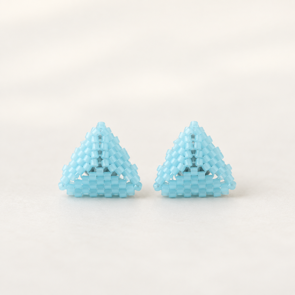 A pair of light blue beaded pyramid stud earrings on a clean, off-white background.