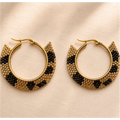 A pair of gold-tone hoop earrings with a semi-circular fringe detail woven with black and gold seed beads, displayed on a textured beige fabric background.