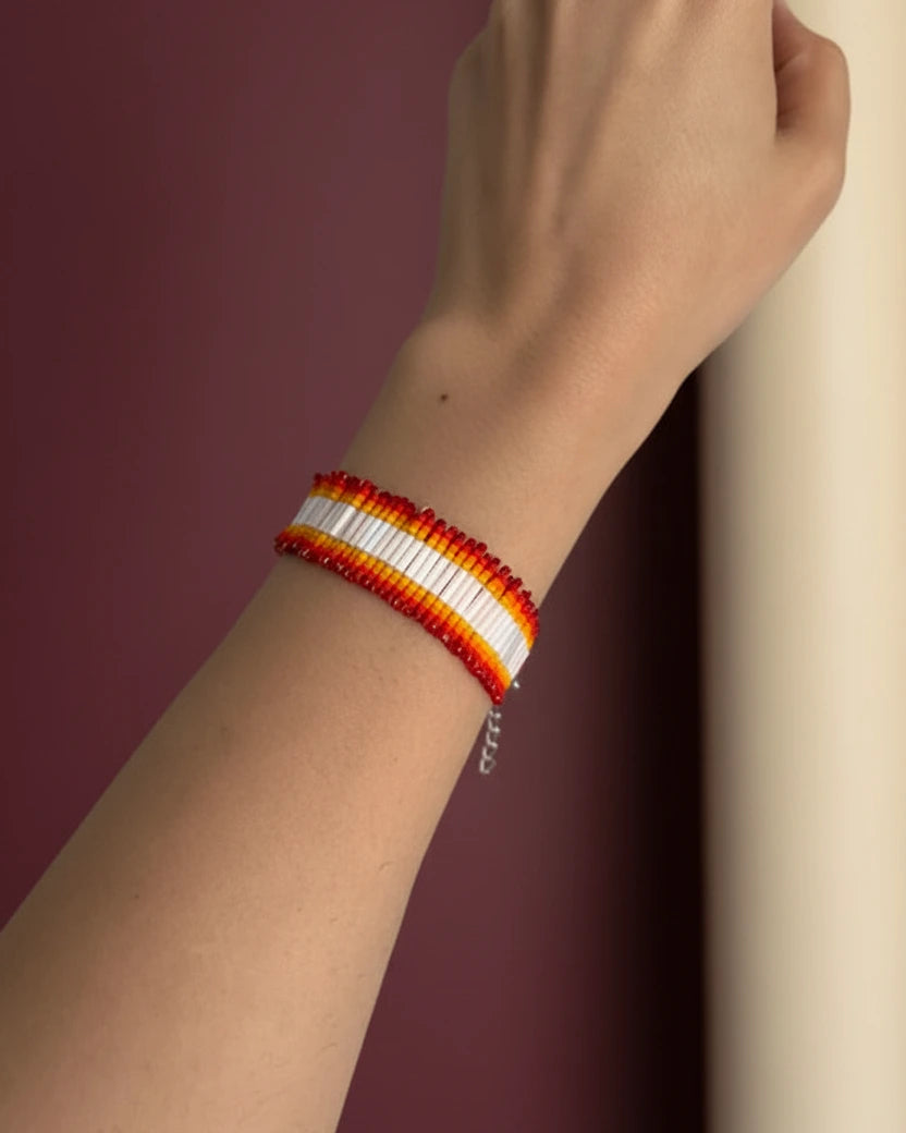 Hand wearing a red, yellow, and white beaded bracelet against a light gray background