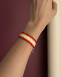 Hand wearing a red, yellow, and white beaded bracelet against a light gray background