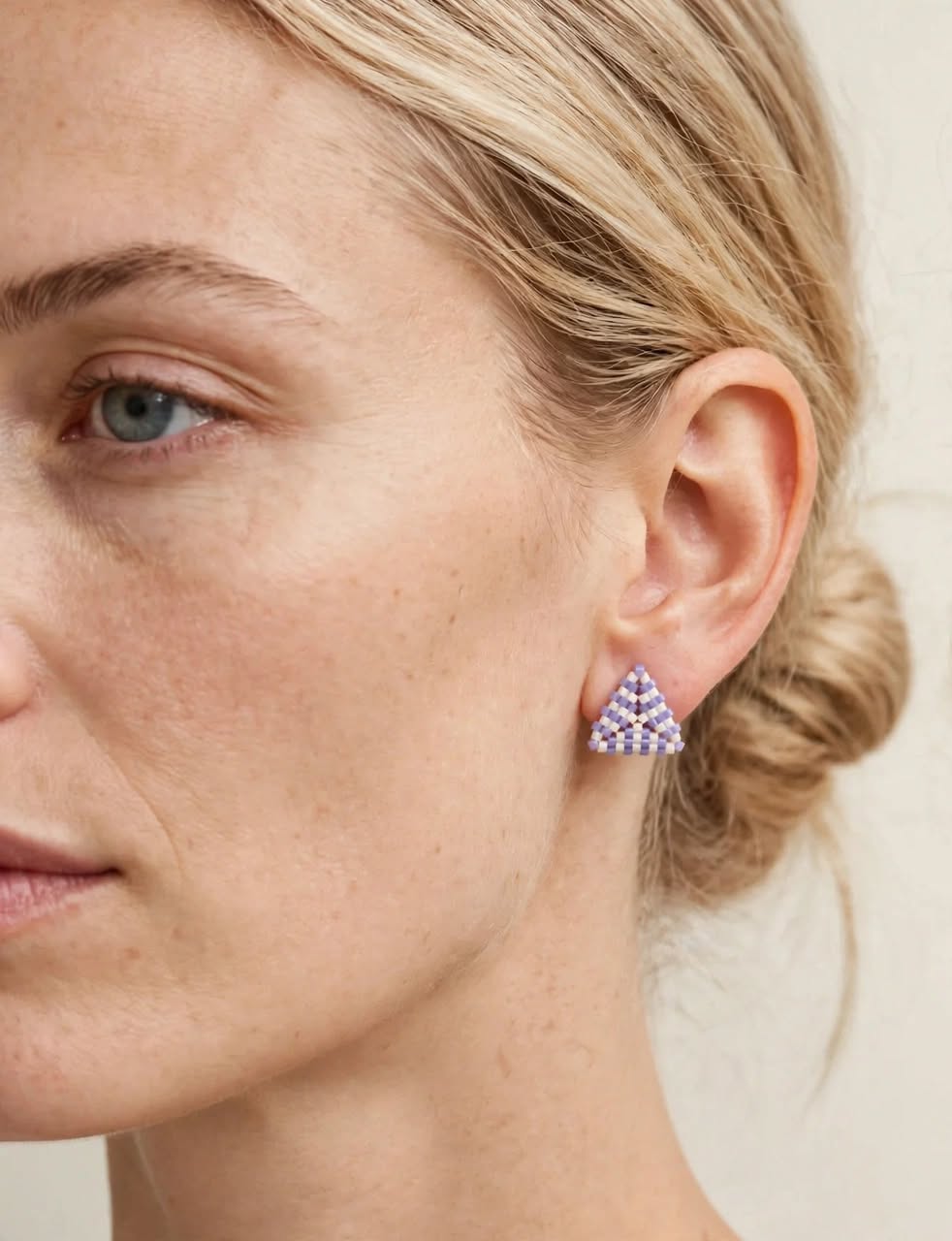 A close-up of a woman's ear wearing a small triangular stud earring with a purple and white geometric pattern.