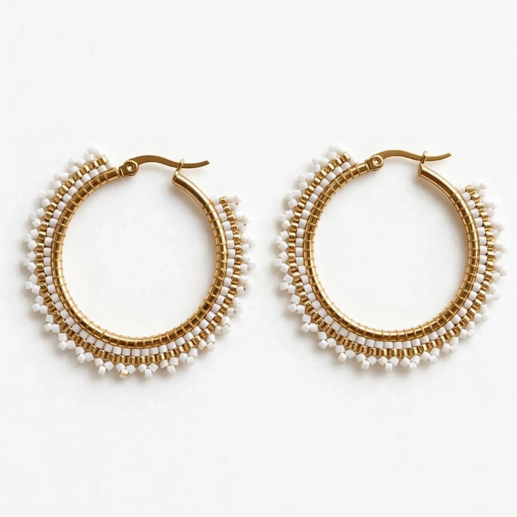 A pair of gold hoop earrings adorned with multiple rows of small white pearls, displayed on a clean white background.
