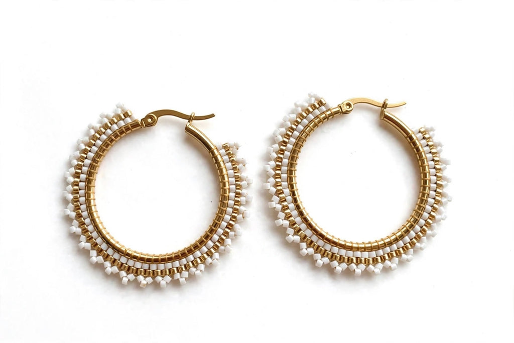 A pair of gold hoop earrings decorated with multiple rows of small white beads, displayed on a clean white background.