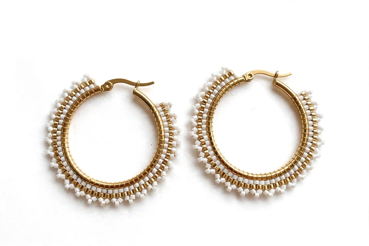 A pair of gold hoop earrings decorated with multiple rows of small white beads, displayed on a clean white background.
