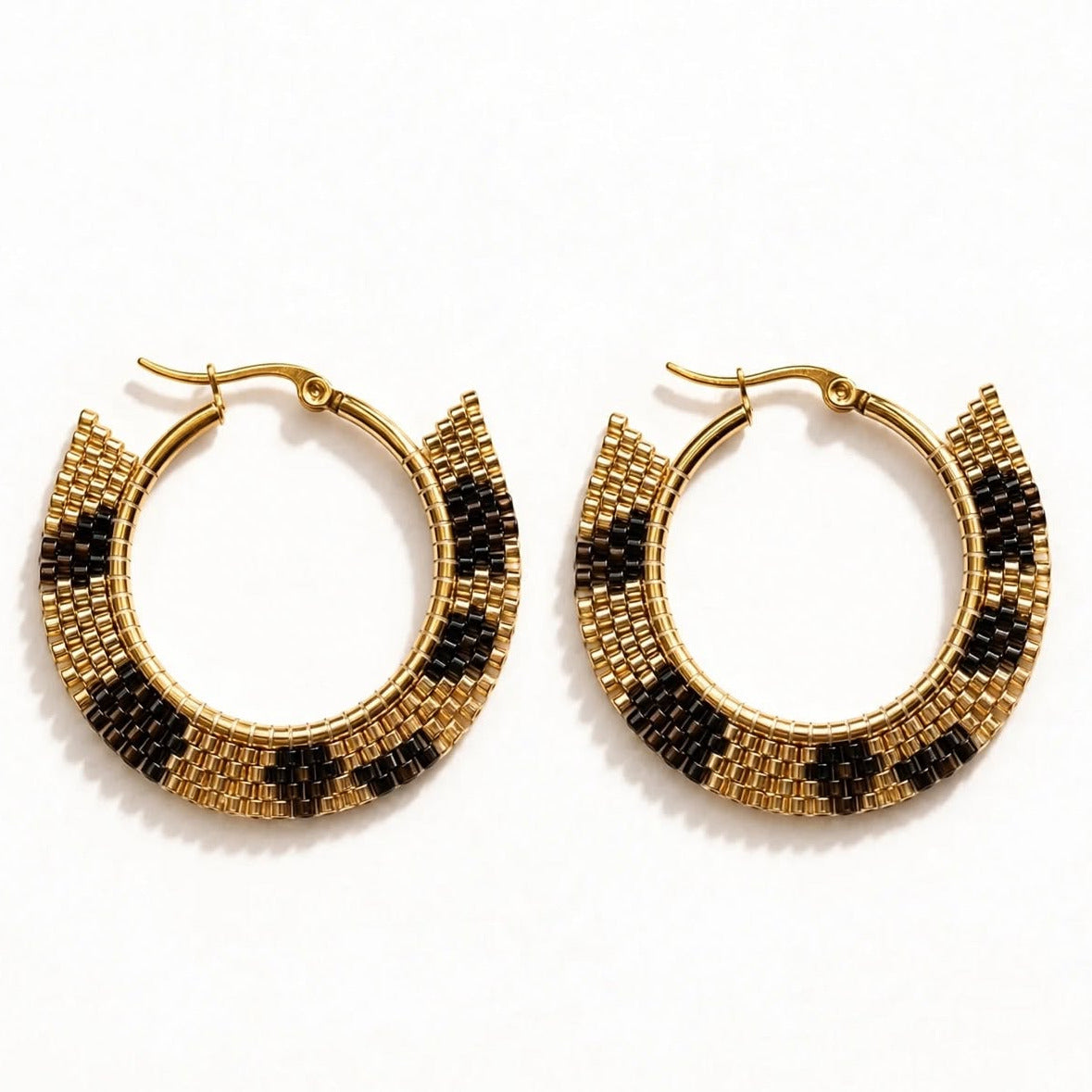 A pair of gold-tone hoop earrings with a textured, scalloped edge featuring alternating rows of small gold and black beads, displayed on a clean white background.