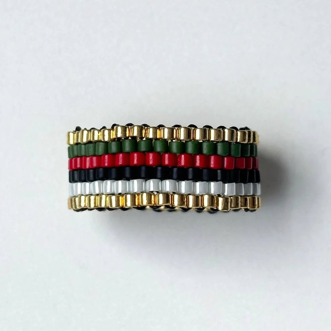 A beaded wrap bracelet featuring horizontal stripes of green, red, black, white, and gold metallic beads, displayed on a clean white background.