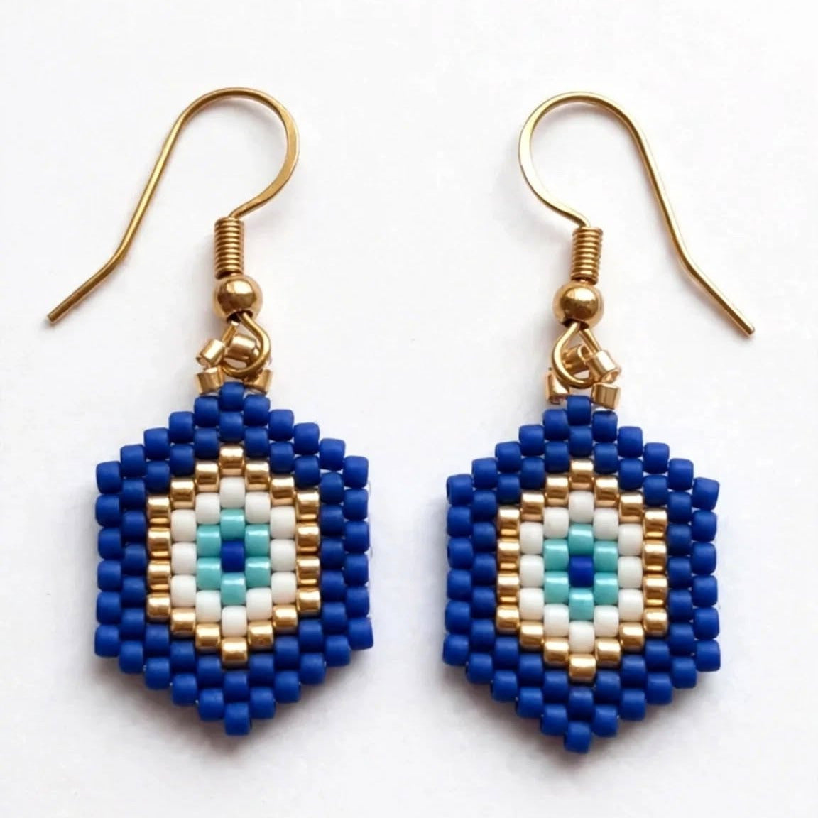 A pair of handmade beaded dangle earrings with blue, white, and light blue evil eye motifs hanging from gold-tone fishhook wires on a plain white background.