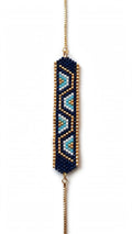 A beaded geometric stretch bracelet featuring a navy blue base with light blue and gold patterned accents, suspended from a gold chain on a white background.