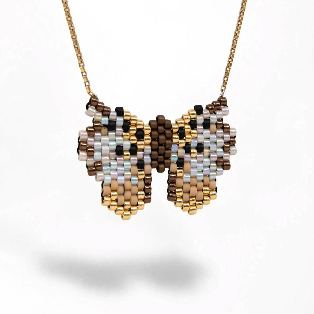 A gold chain necklace with a butterfly-shaped beaded pendant, featuring a pattern of brown, beige, white, and light blue seed beads, shown against a plain white background.