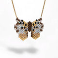 A gold chain necklace with a butterfly-shaped beaded pendant, featuring a pattern of brown, beige, white, and light blue seed beads, shown against a plain white background.