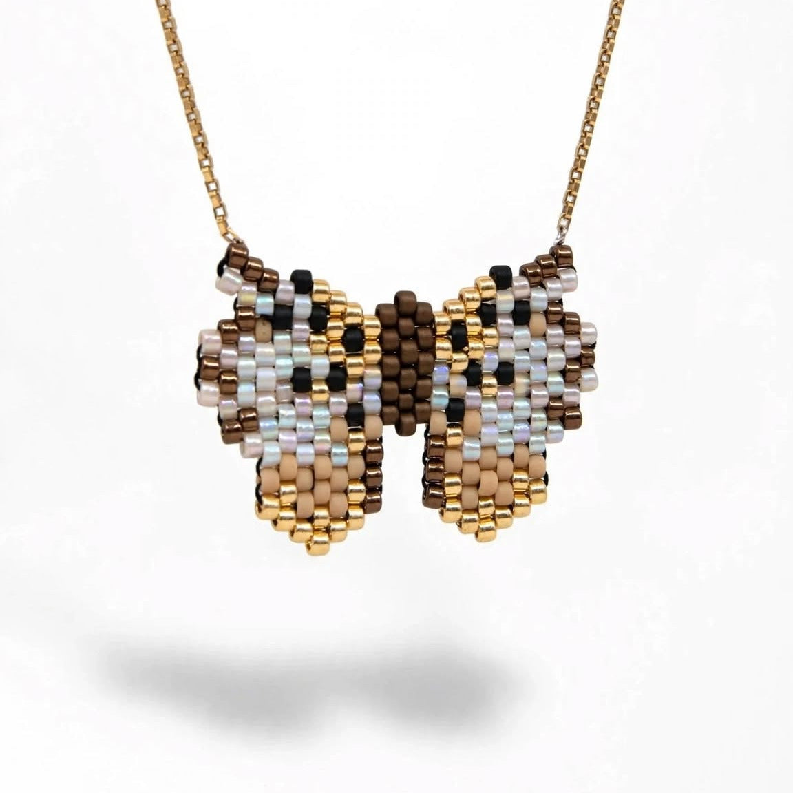 A gold chain necklace with a butterfly-shaped beaded pendant, featuring a pattern of brown, beige, white, and light blue seed beads, shown against a plain white background.