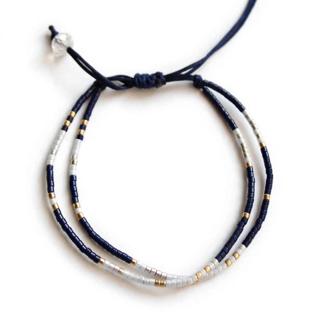 A beaded adjustable cord bracelet featuring dark navy blue cords, white beads, and small gold spacer beads, shown on a plain white background.