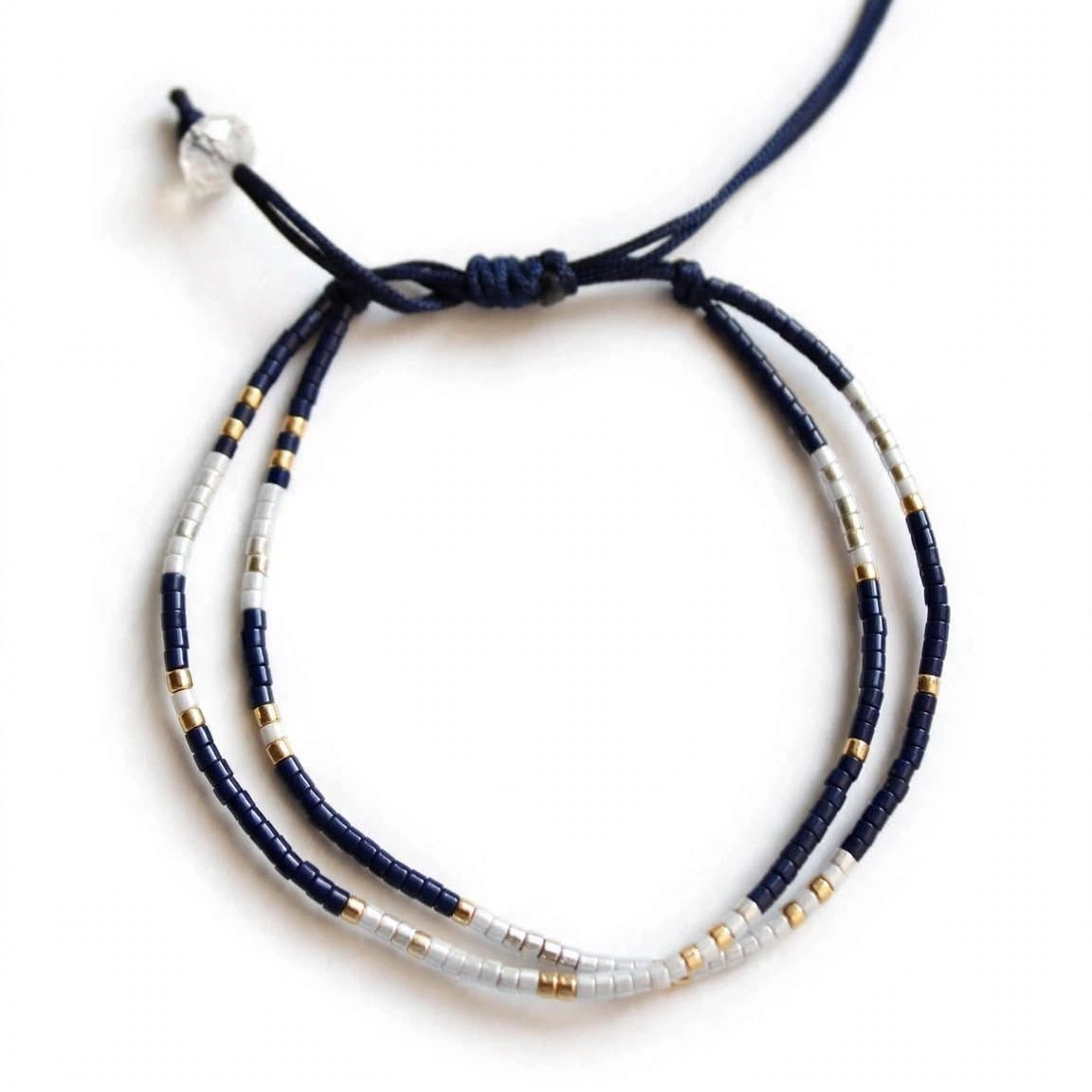 A beaded adjustable cord bracelet featuring dark navy blue cords, white beads, and small gold spacer beads, shown on a plain white background.