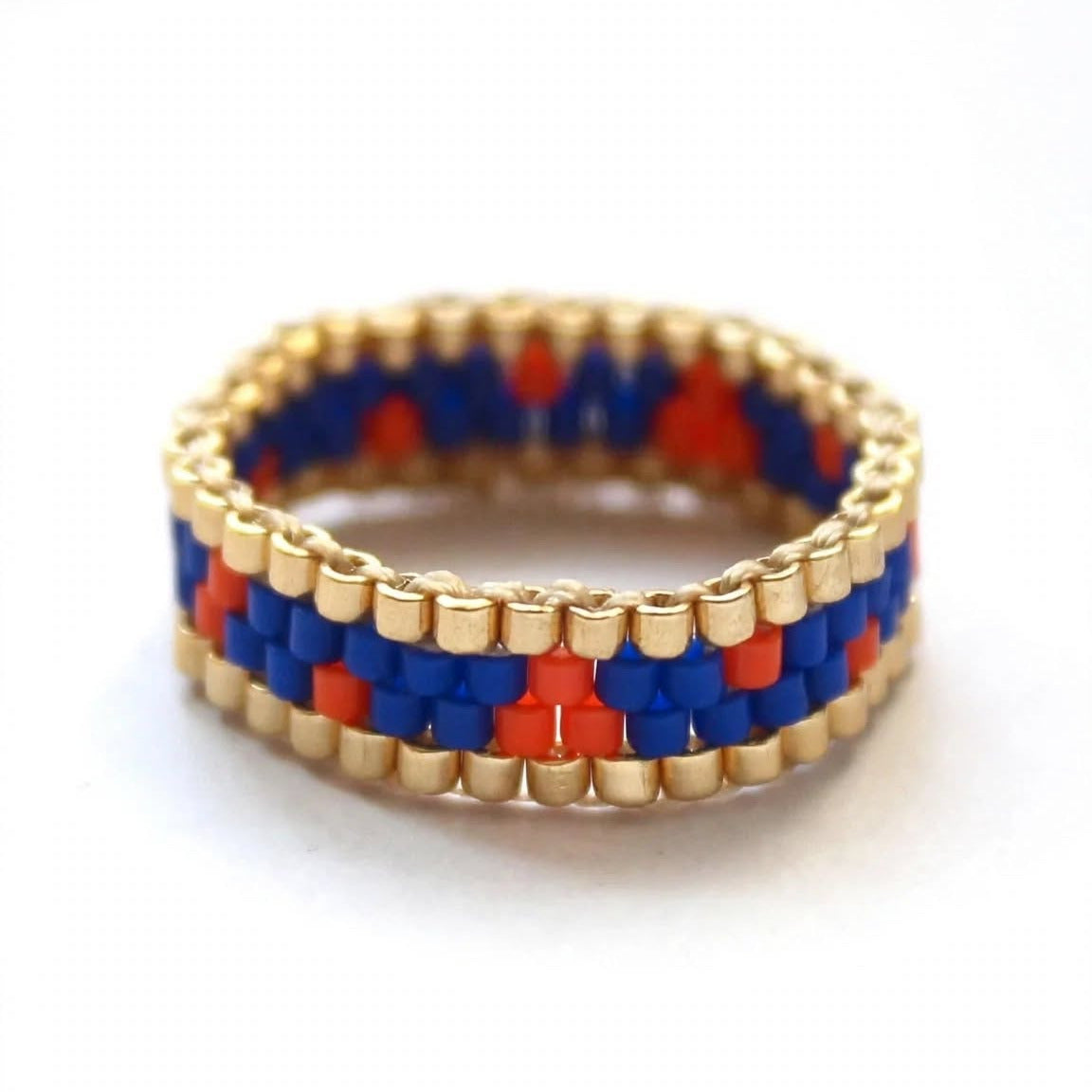 A beaded ring with a geometric pattern of red, blue, and gold seed beads, photographed on a clean white background.