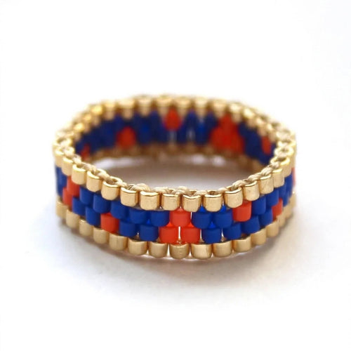 A beaded ring with a geometric pattern of red, blue, and gold seed beads, photographed on a clean white background.