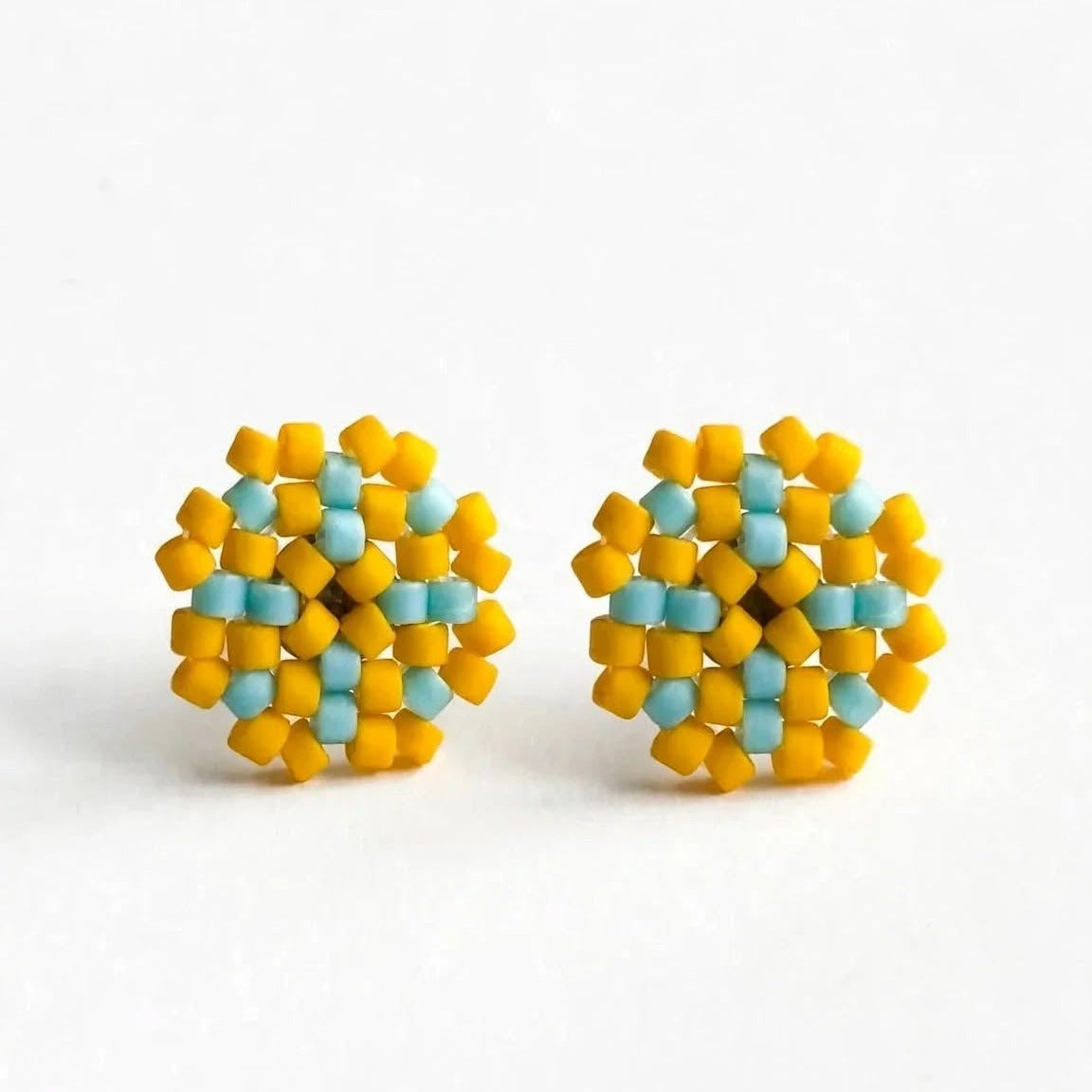 A pair of handmade beaded stud earrings with a geometric pattern of yellow and light blue beads, displayed on a clean white background.