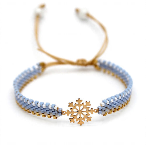 A beaded adjustable cord bracelet featuring light blue and white beads, a gold-toned snowflake charm in the center, and a gold-toned sliding cord clasp, shown on a plain white background.