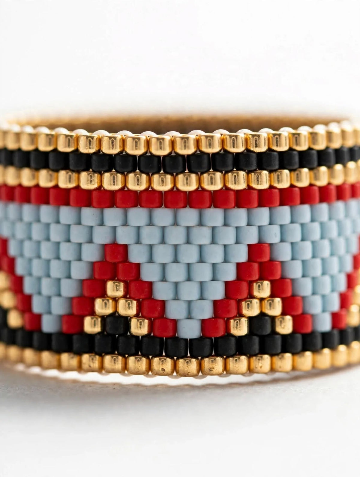A close-up of a beaded wrap bracelet featuring a geometric pattern with light blue, red, black, and gold seed beads.