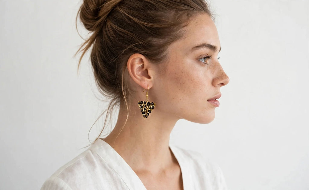A woman in profile wearing a gold and black beaded triangular dangle earring, photographed against a clean white background.