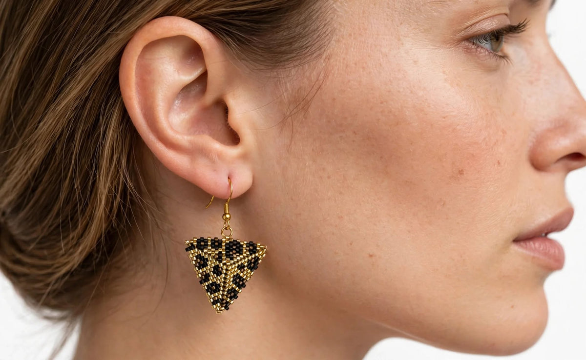 A close-up side profile of a woman wearing a dangling triangular beaded earring in black and gold.