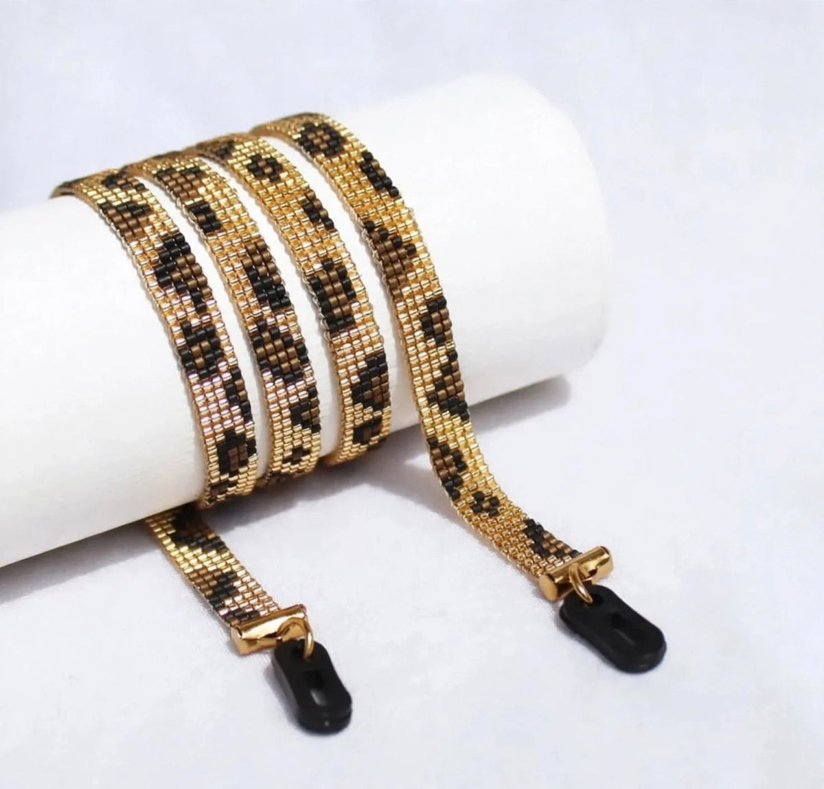 Beaded strap with gold and black pattern on a white cylindrical object against a light gray background