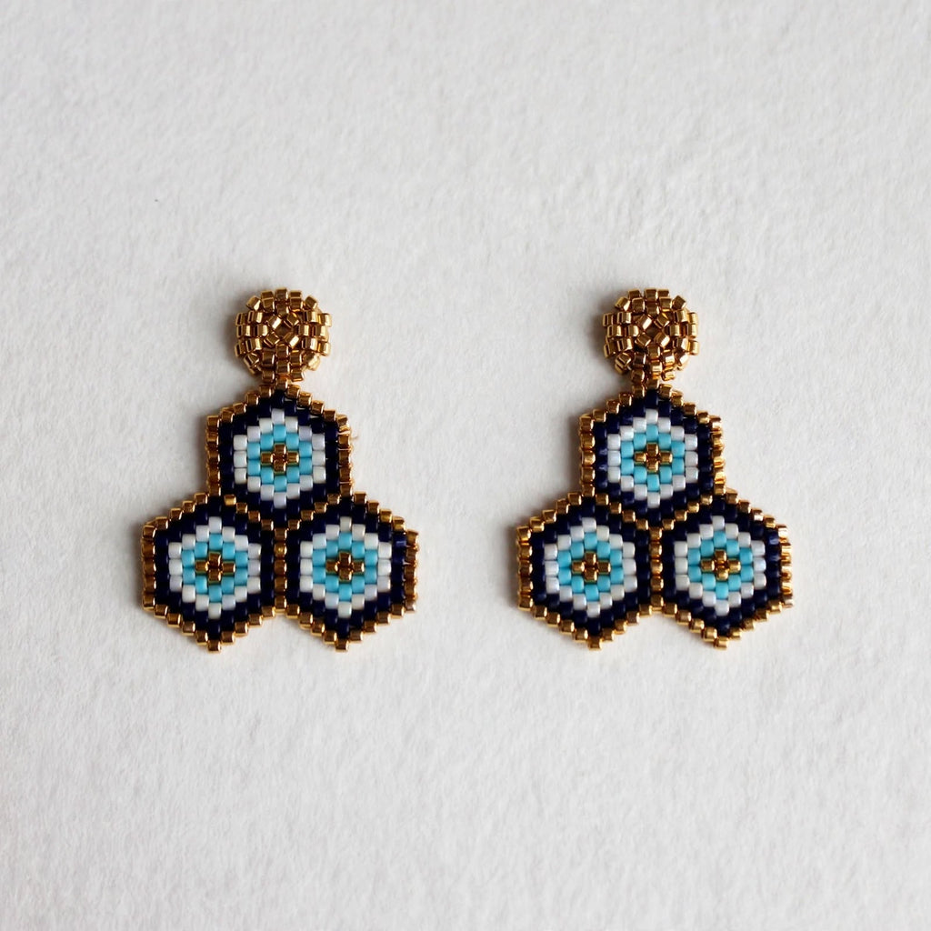 A pair of handmade beaded geometric dangle earrings featuring three nested hexagonal motifs in light blue, white, and black, finished with textured gold-tone studs, displayed on a clean white background.