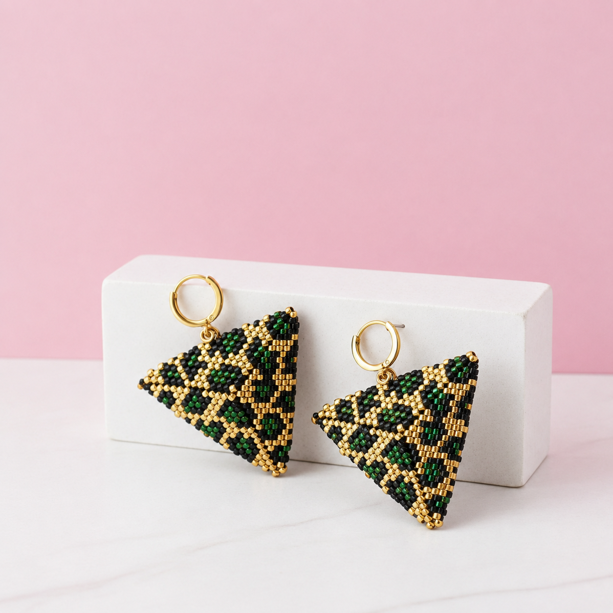 Triangular beaded earrings on a white stand with a pink background