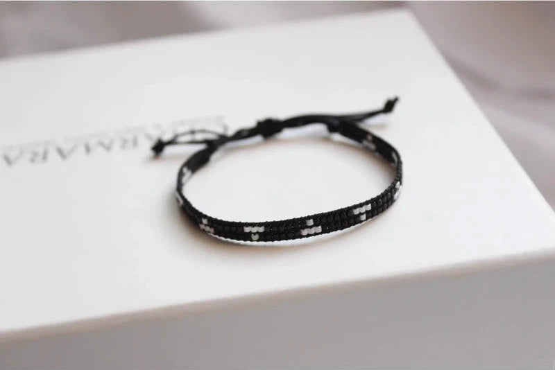 Black woven bracelet on a white surface with a blurred background