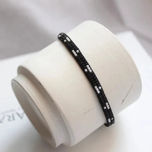 Black beaded bracelet on a white cylindrical stand with 'AR' branding.