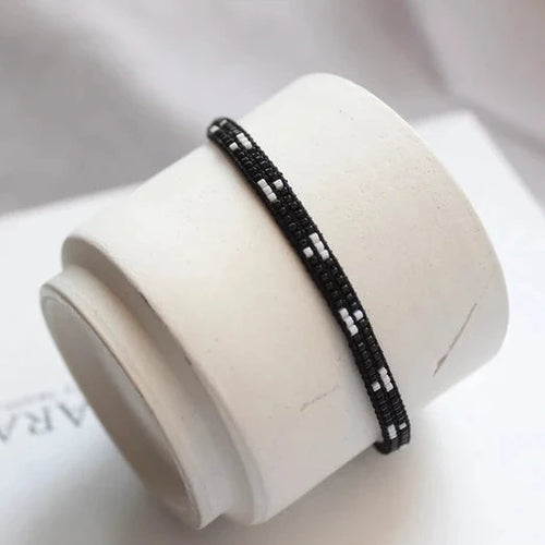 Black beaded bracelet on a white cylindrical stand with 'AR' branding.