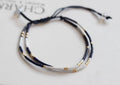 Two layered bracelets with black, white, and gold beads on a light background