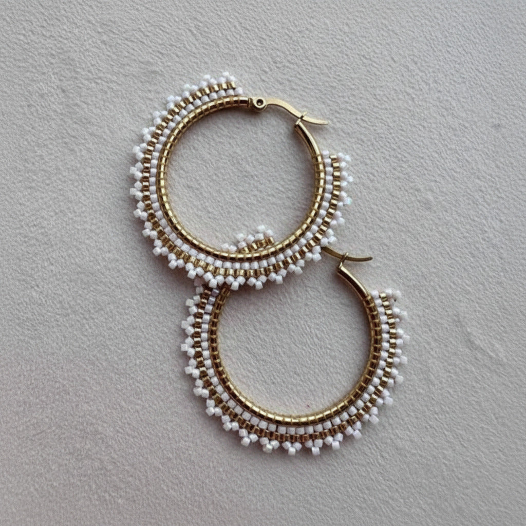 Pair of gold hoop earrings with white bead detailing on a gray background