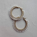 Pair of gold hoop earrings with white bead detailing on a gray background